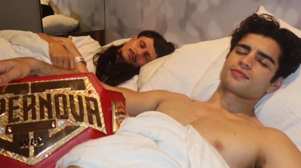 Two Men Asleep in a Bed with White Sheets; One Wears a Hospital Wristband and a Large Gold Wrestling Championship Belt Lies in the Foreground. • Guadalupe Informa