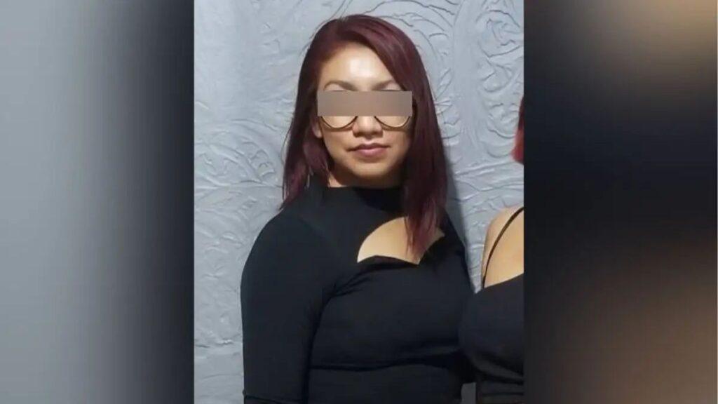 Entrevista-de-trabajo-lizbeth • Guadalupe Informa Woman with Burgundy Hair in a Black Top Featuring a Chest Cutout, Standing Against a Textured Gray Wall; Eyes Obscured by a Blur. • Guadalupe Informa