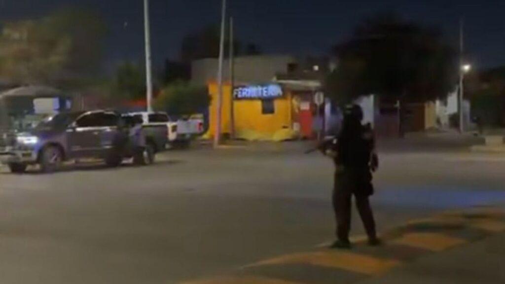 Nighttime Street with a Silhouetted Armed Officer Standing on a Curb As Police Suvs Drive By; Orange Storefront in Background. • Guadalupe Informa