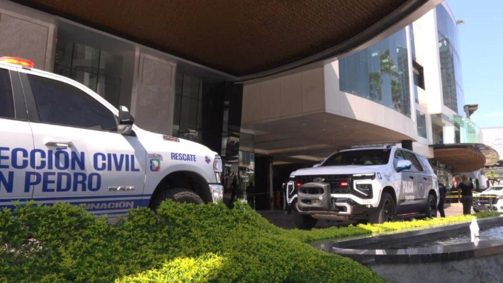 Two White Emergency Vehicles (police Suv and Rescue Van) Parked at the Entrance of a Modern Glass-front Building, with Green Shrubs in the Foreground. • Guadalupe Informa